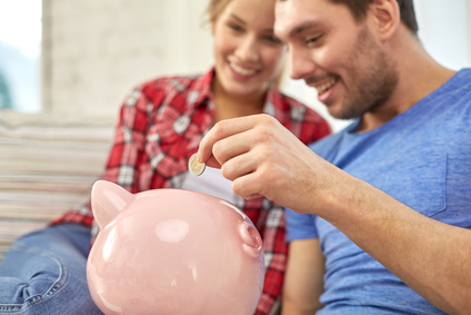 money, home, finance and relationships concept - close up of couple with piggy bank sitting on sofa